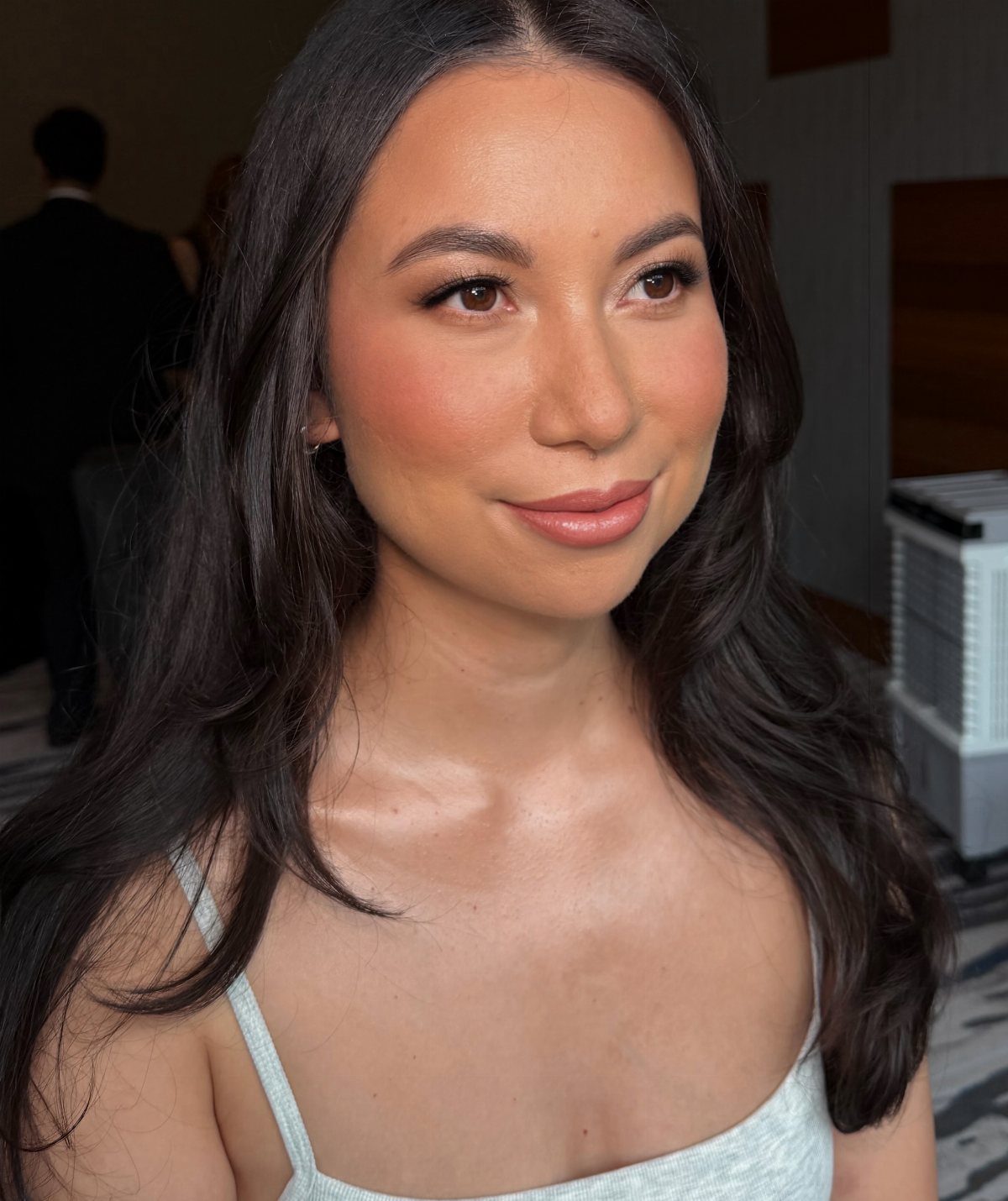 Asian woman with soft glam makeup, peach blush, and long dark wavy hair.