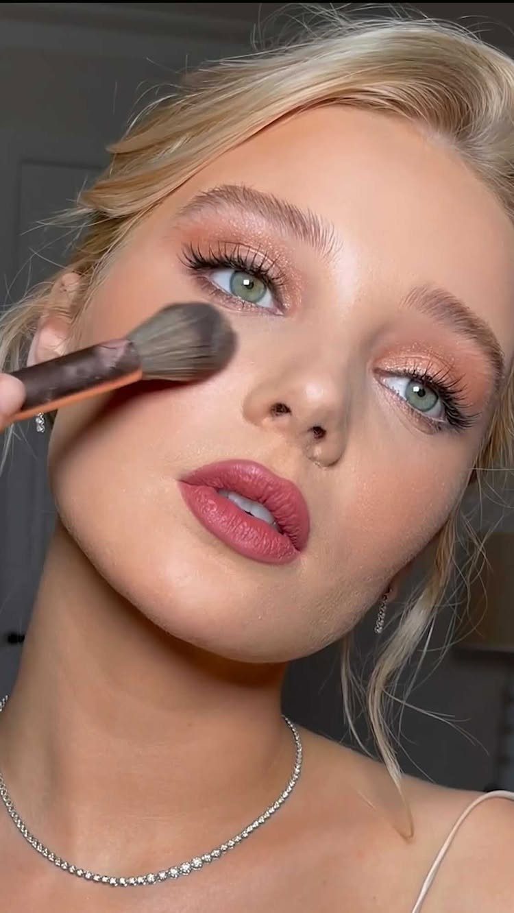 Woman with bridal makeup and peach eyeshadow having powder applied with a brush