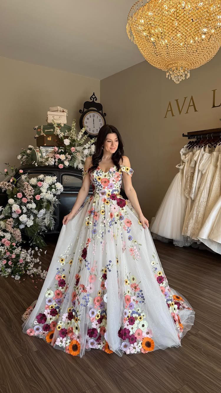 Woman in a white wedding dress with colorful 3D floral appliqués in a boutique.