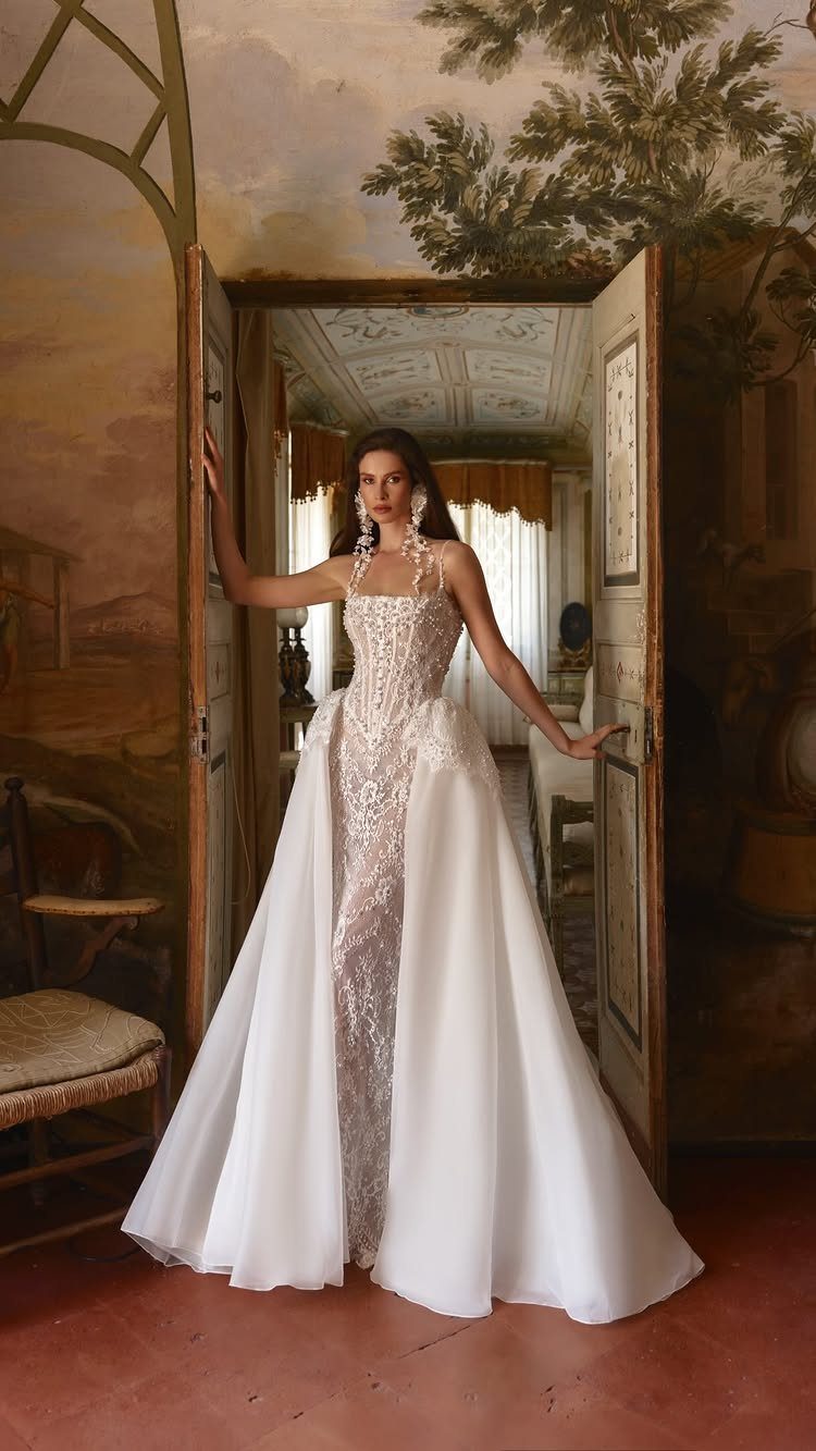 Woman in a white beaded wedding dress with a full overskirt standing in a doorway