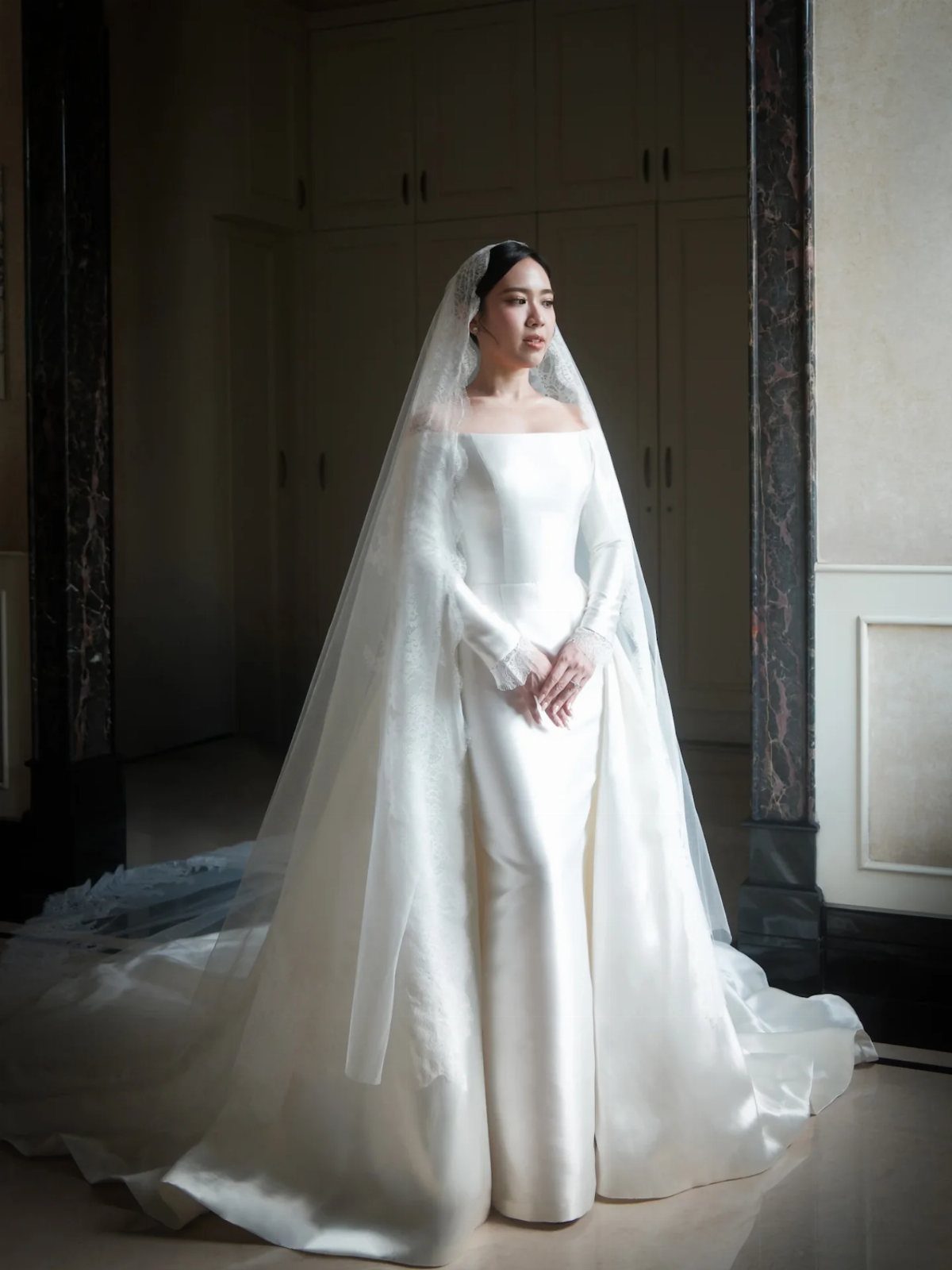 Woman in a sleek off-the-shoulder white satin wedding dress with a long veil.
