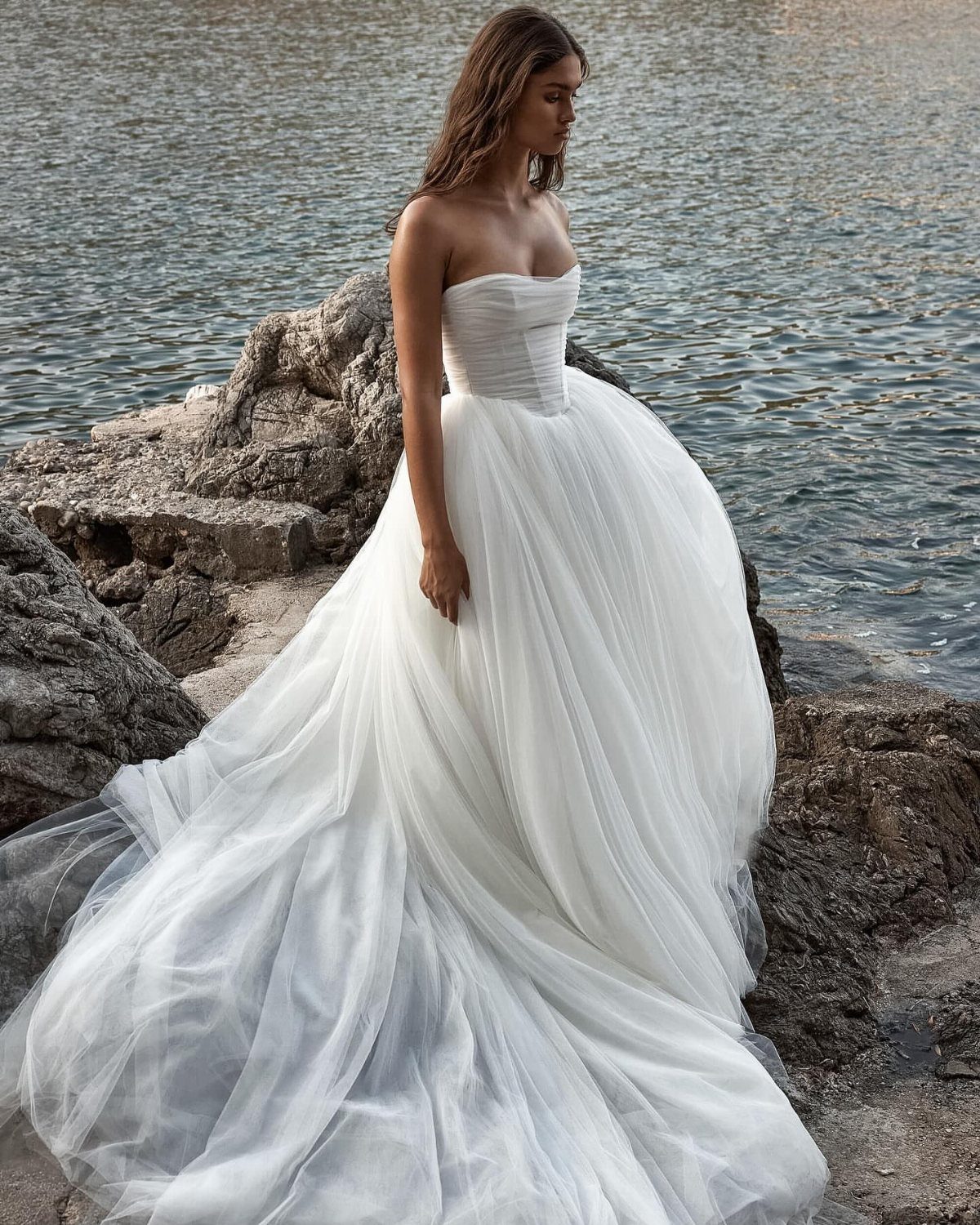 Woman in a strapless white wedding dress with a full tulle skirt on rocky shore