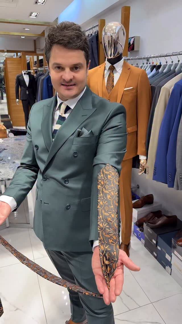 Man wearing a dark green double-breasted suit holding a gold patterned tie in store