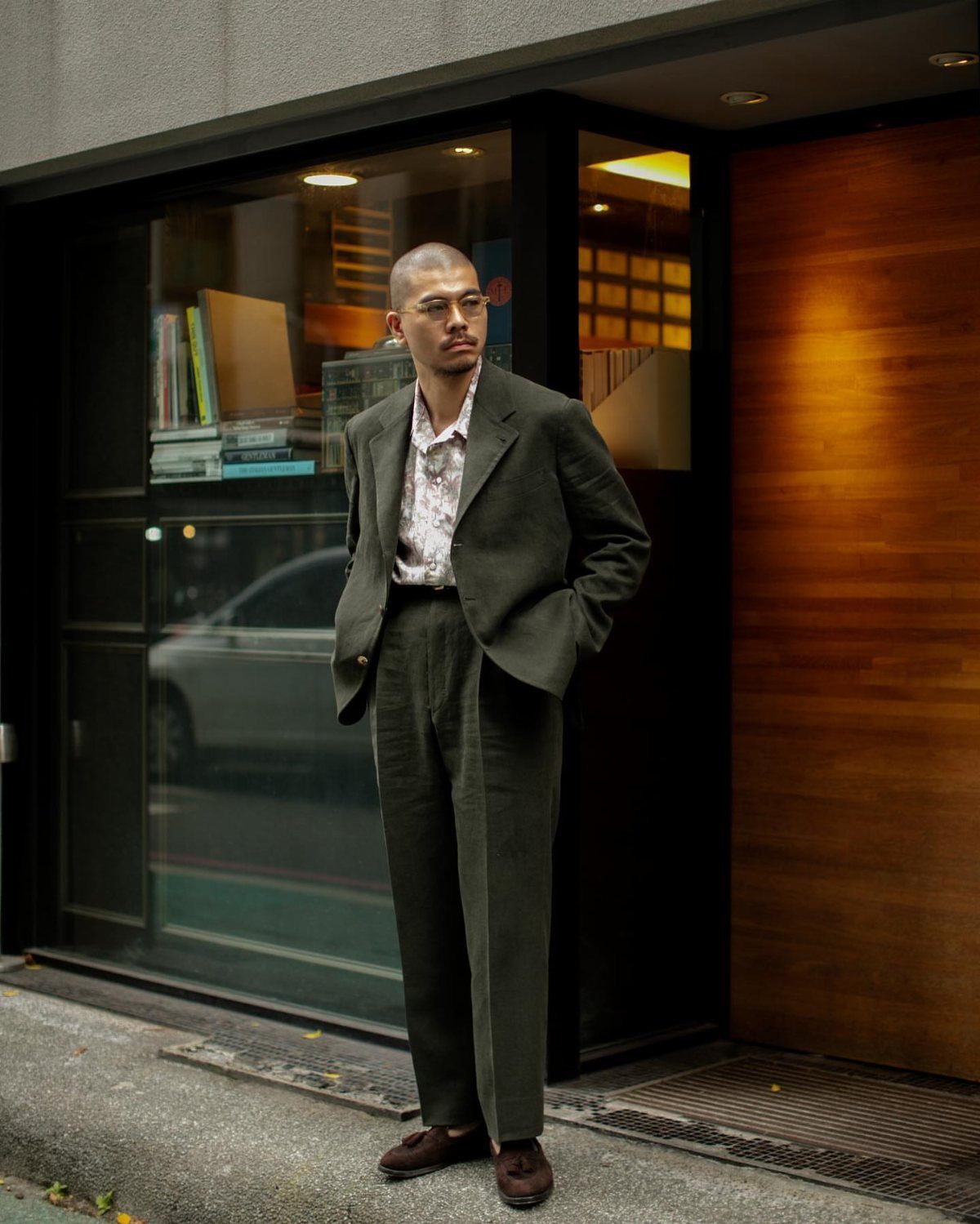 Man wearing a dark olive green suit and brown loafers standing outdoors.