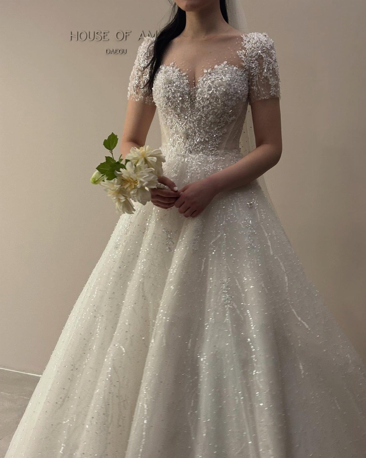Sparkling white bridal gown with sweetheart neckline and short lace sleeves holding white flowers