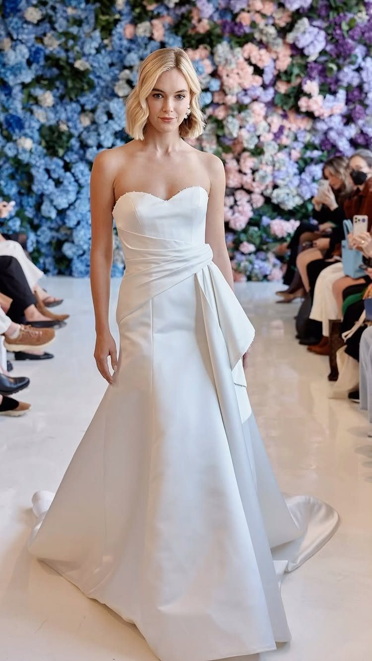 Woman in a white sweetheart neckline wedding dress walking on a floral runway.