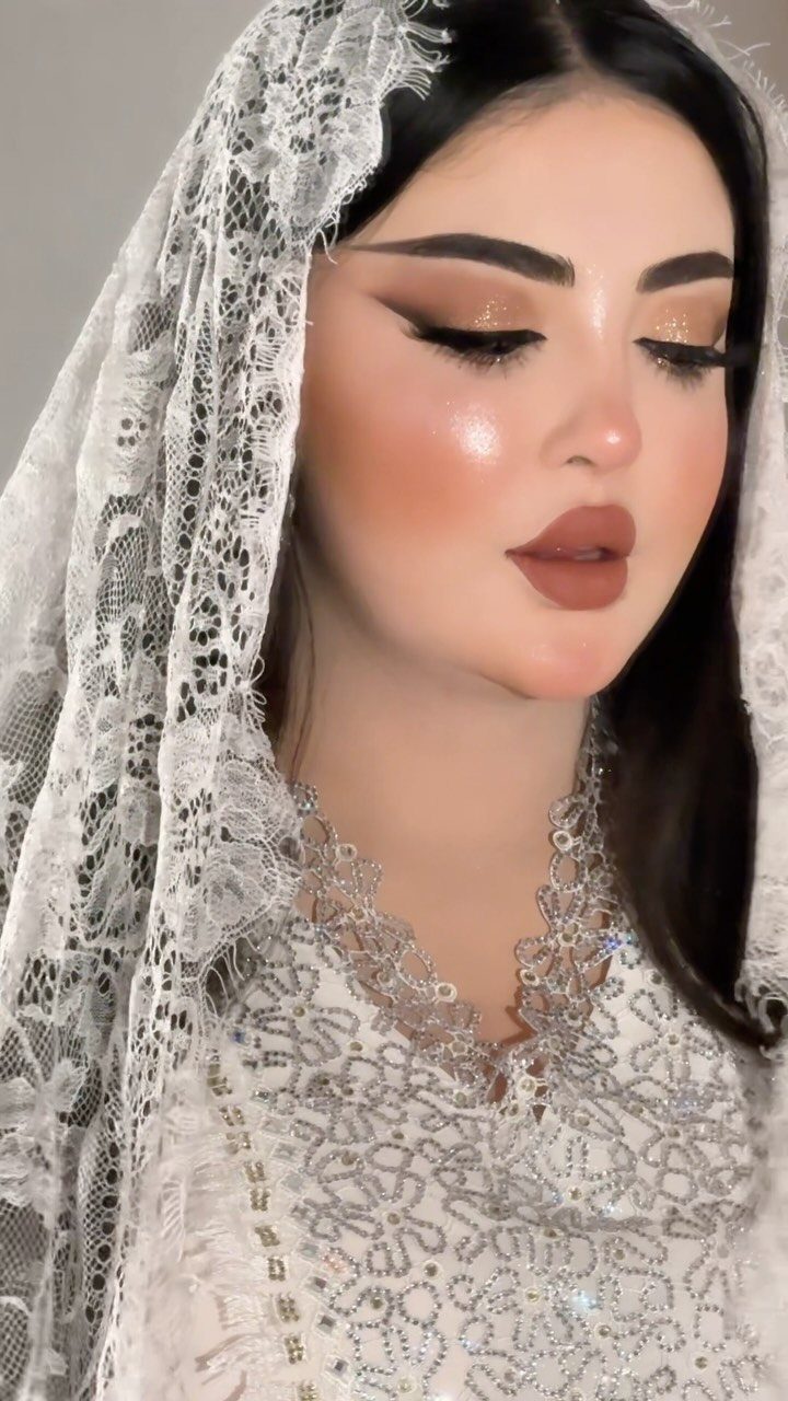 Woman with bold Arabic bridal makeup wearing a white lace veil and dress.