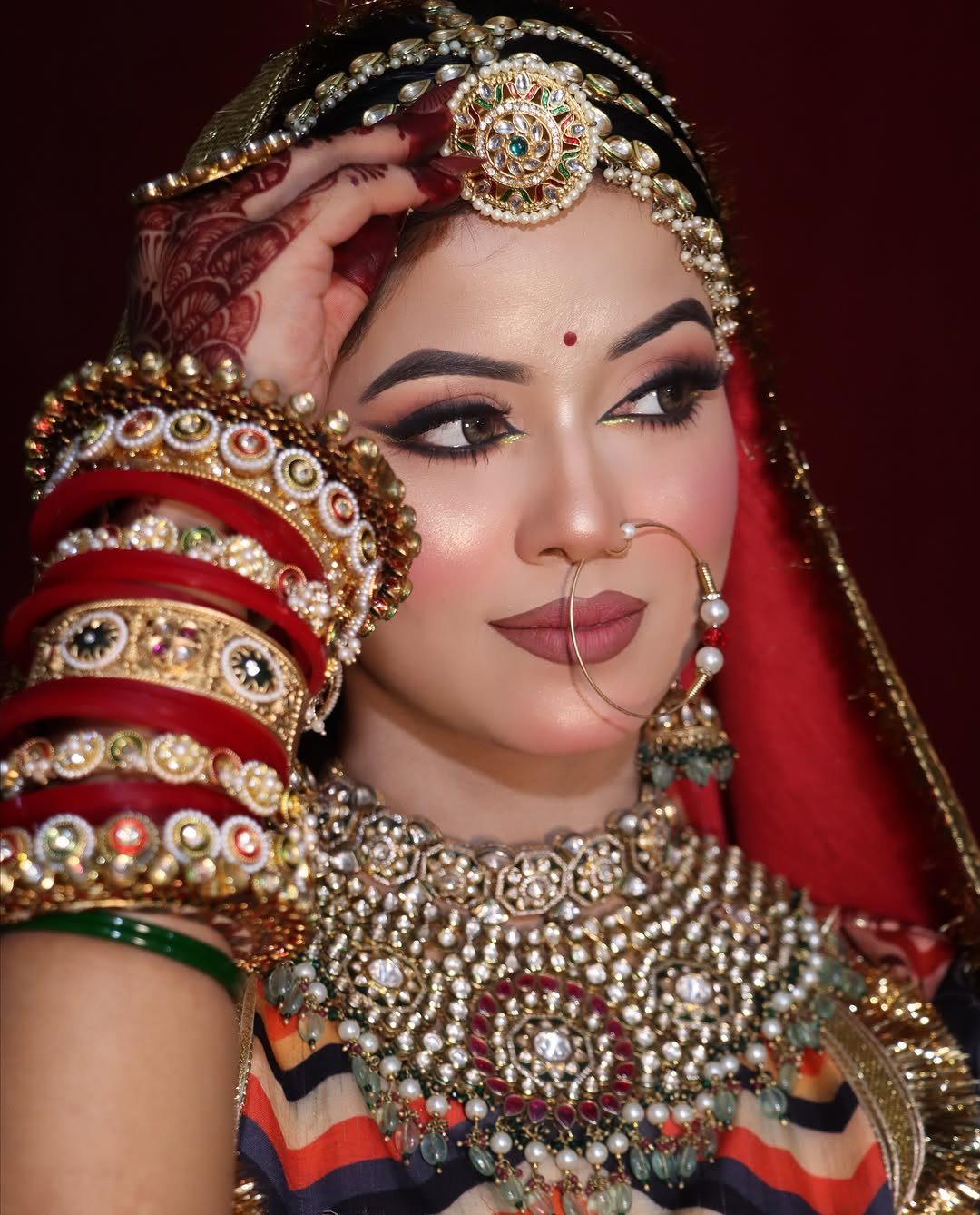 Indian bride with royal makeup, ornate gold jewelry, and a red bridal veil.