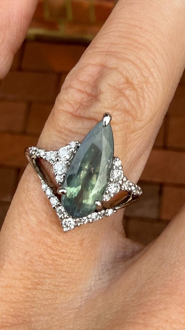 Marquise-cut teal-green alexandrite engagement ring with diamond halo on a person's finger