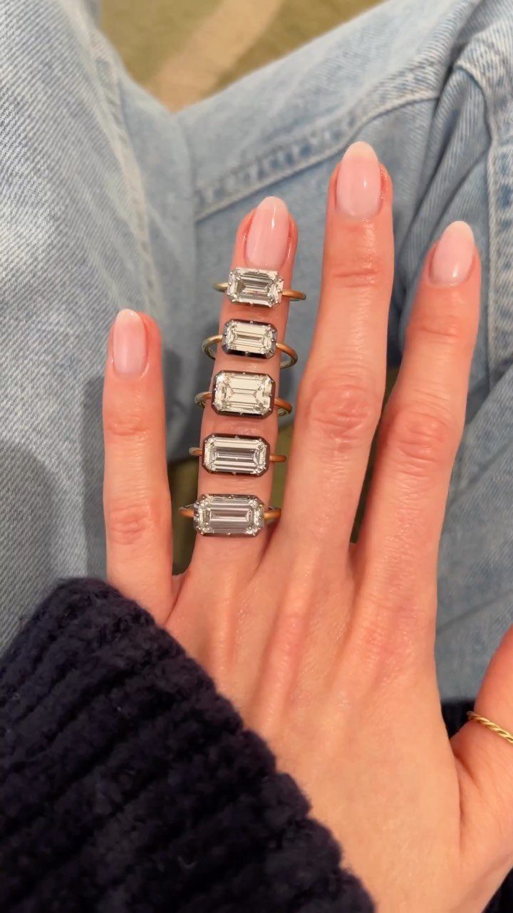 Five emerald-cut diamond rings set horizontally on a woman's finger with pink nails.