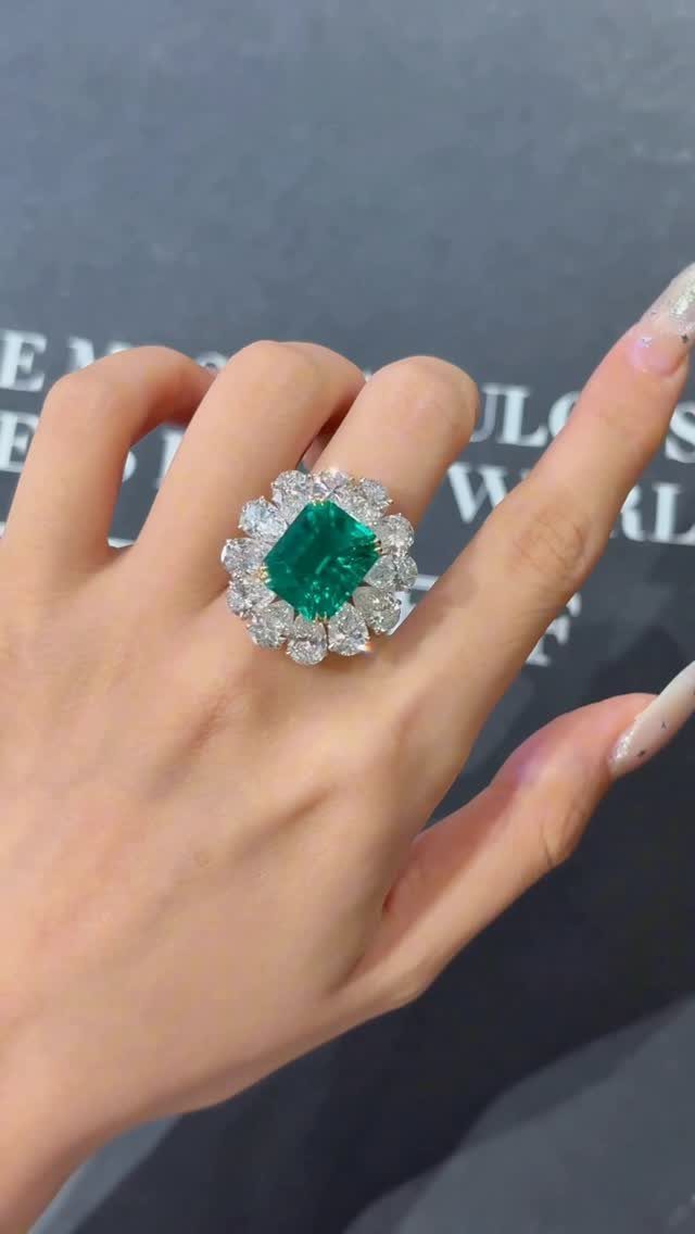Emerald engagement ring with a diamond halo worn on a woman's finger