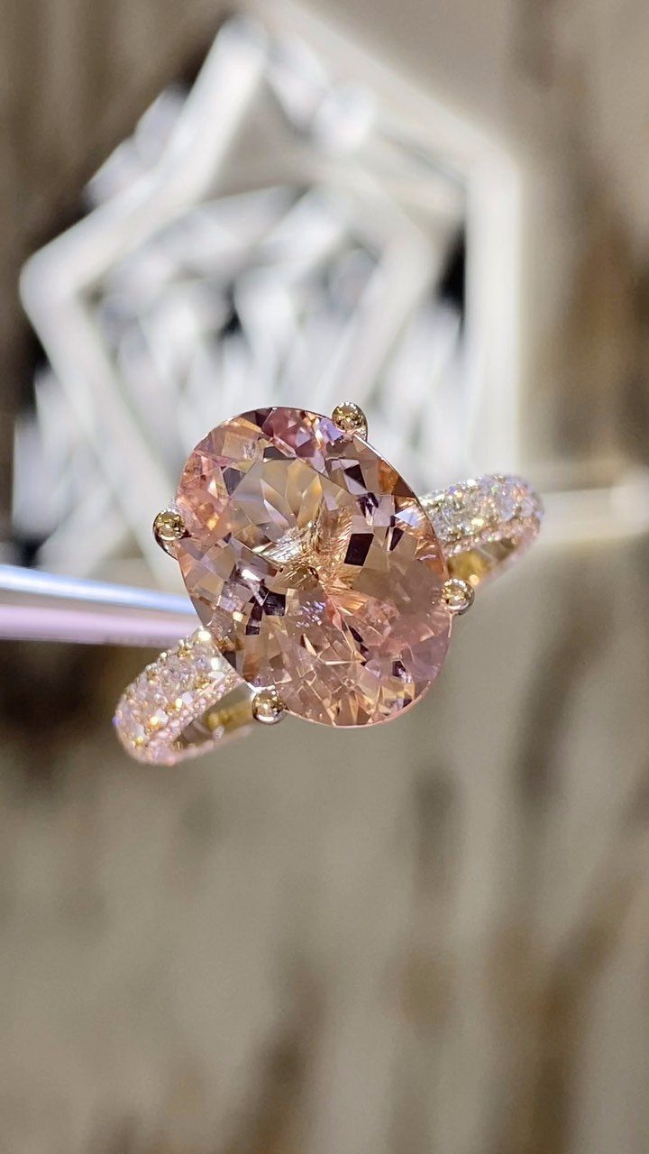 Oval peach-pink morganite engagement ring with a diamond-studded rose gold band.