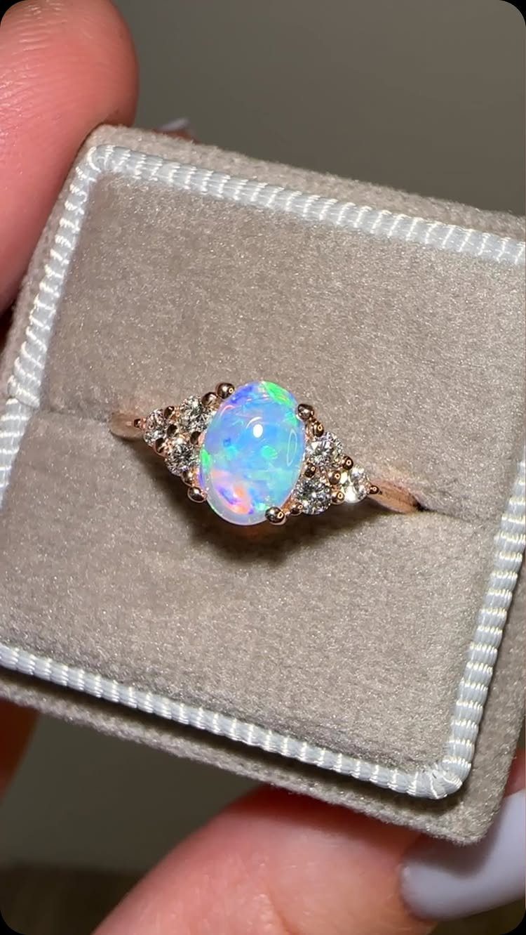Oval opal engagement ring with side diamonds in a grey velvet box