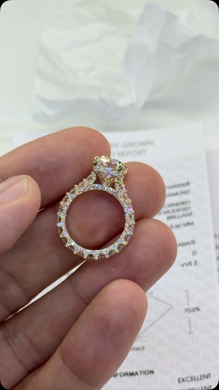 Gold engagement ring with a diamond halo and pavé band held by fingers
