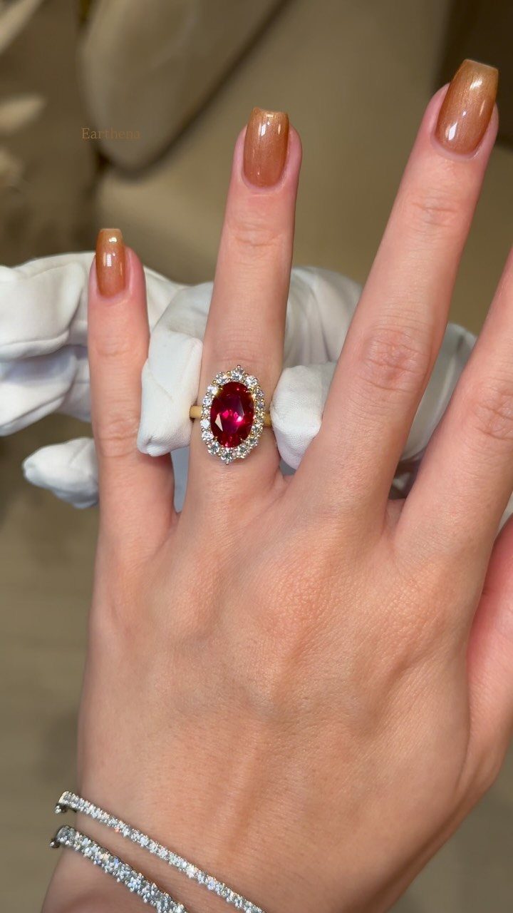 Oval red ruby engagement ring with diamond halo on a woman's finger