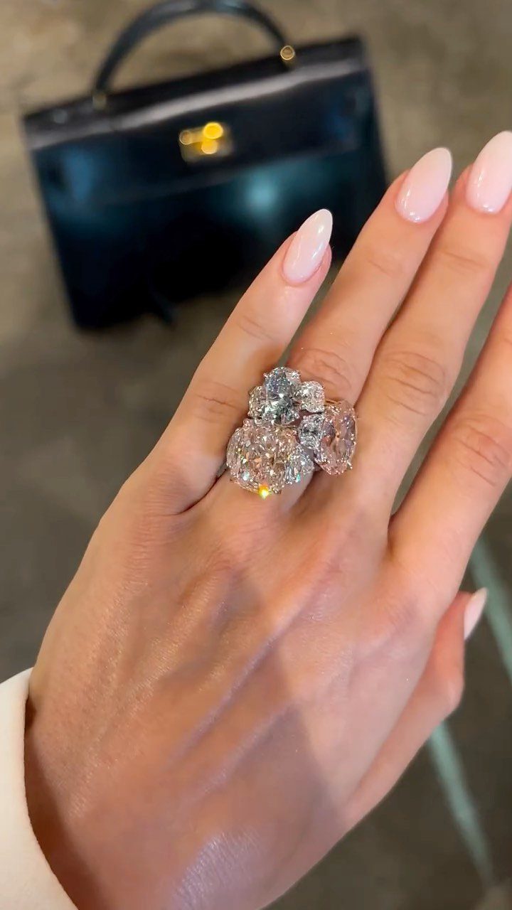 Ornate diamond ring with three large stones on a hand with pink nails