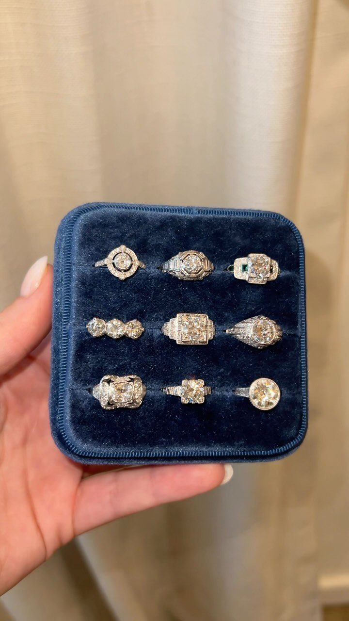 Nine vintage style engagement rings displayed in a navy blue velvet jewelry box.