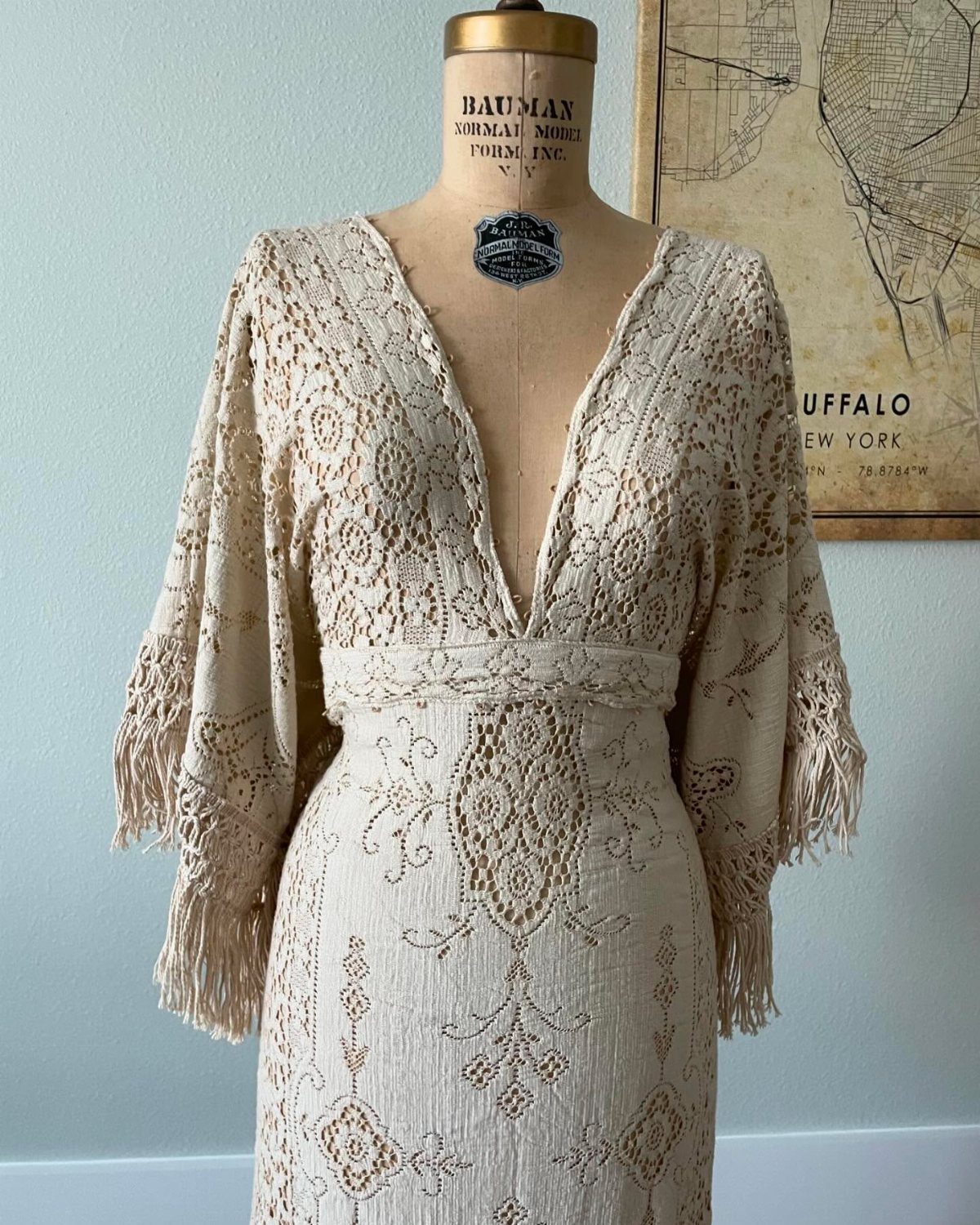 Cream vintage lace wedding dress with fringed sleeves on a tailor's mannequin