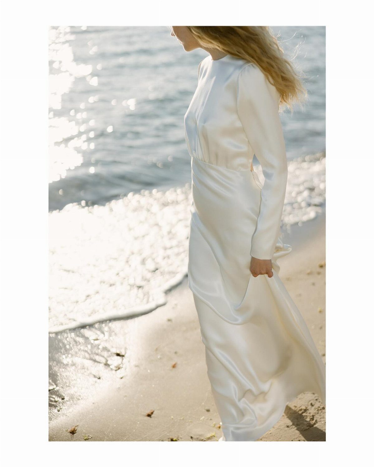 Woman in a minimalist white silk wedding dress standing on a sunny beach