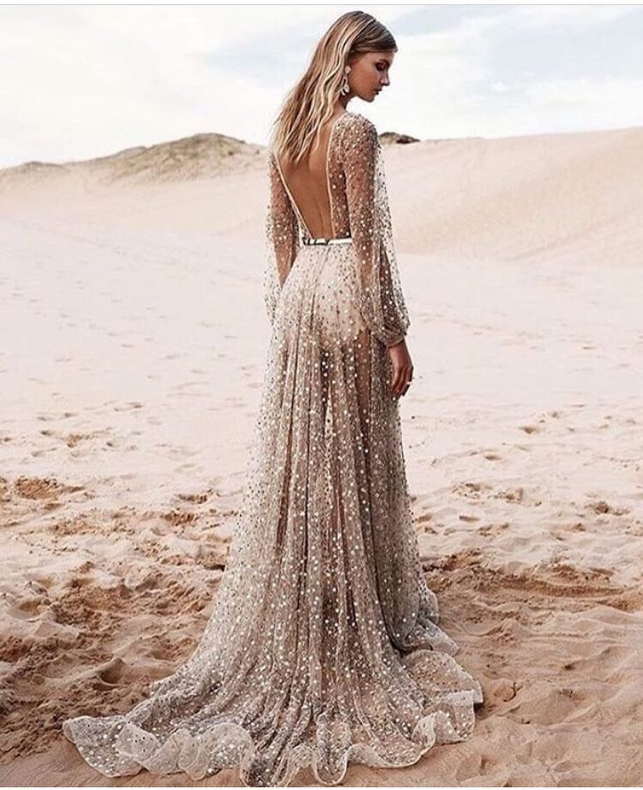 Woman in a shimmering champagne wedding gown standing on a sandy beach