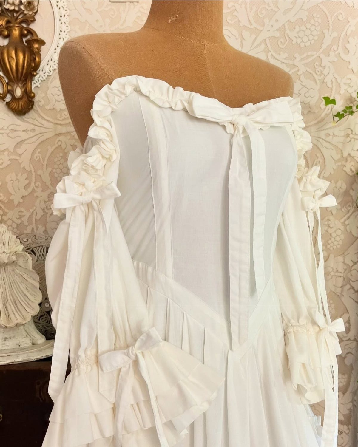 White vintage wedding dress with ruffles and bows on a tan mannequin