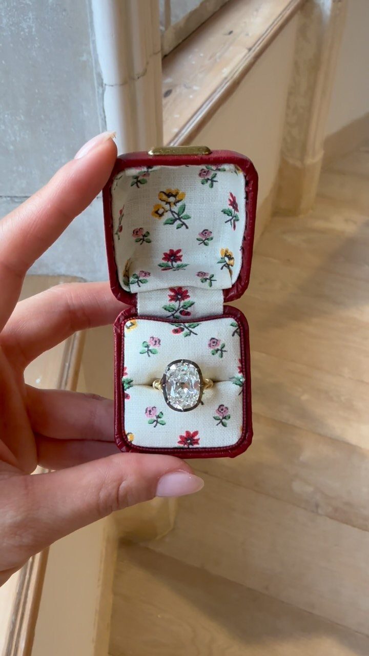Gold ring with oval diamond in a red floral ring box held by hand