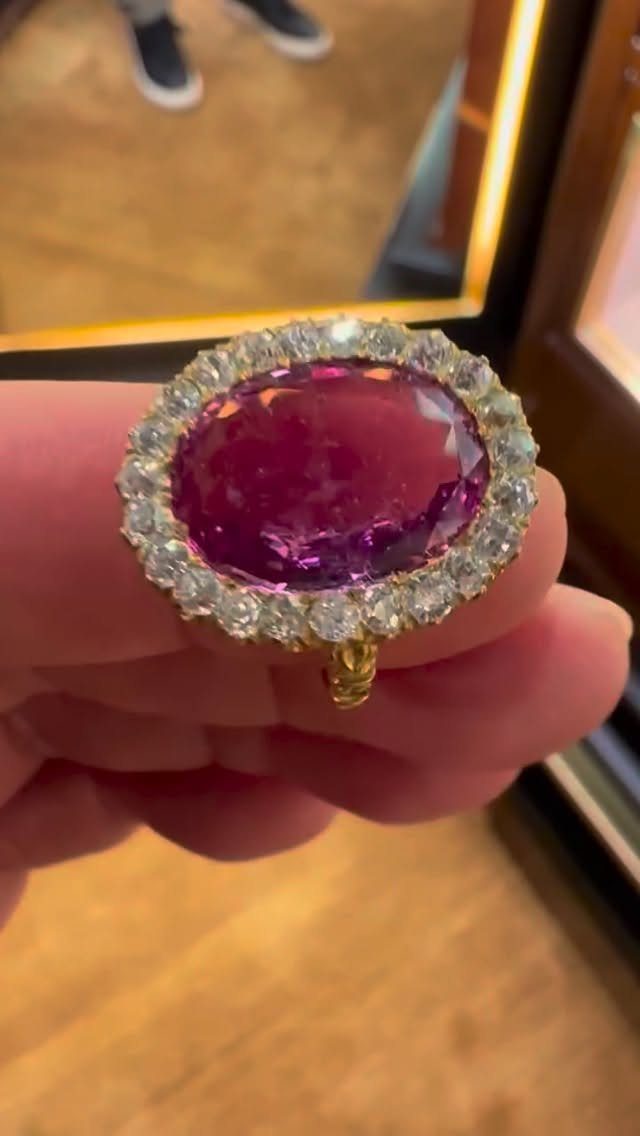 Gold ring with a large oval purple gemstone surrounded by a diamond halo.