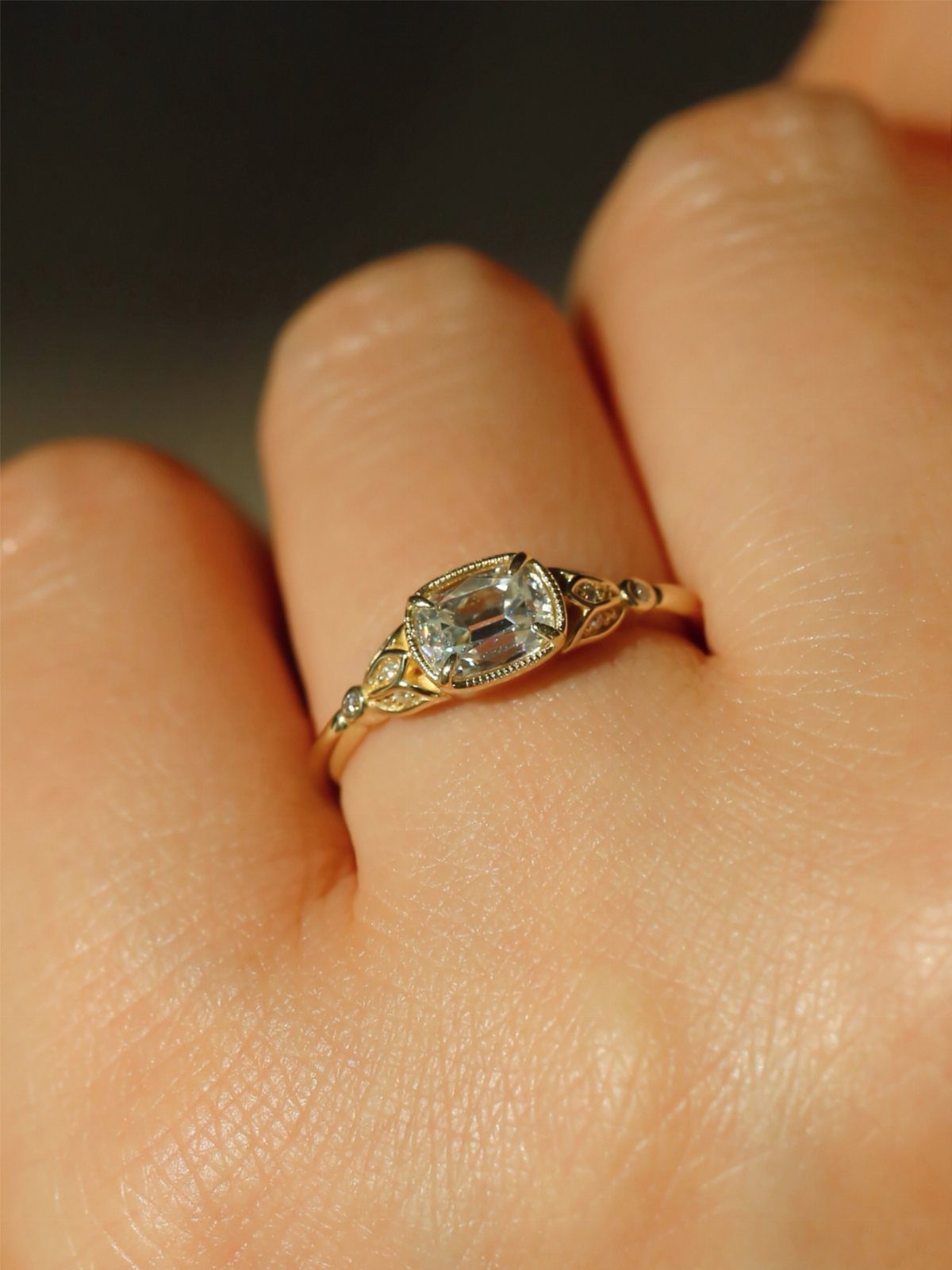 Gold vintage style diamond ring with emerald cut stone on a finger