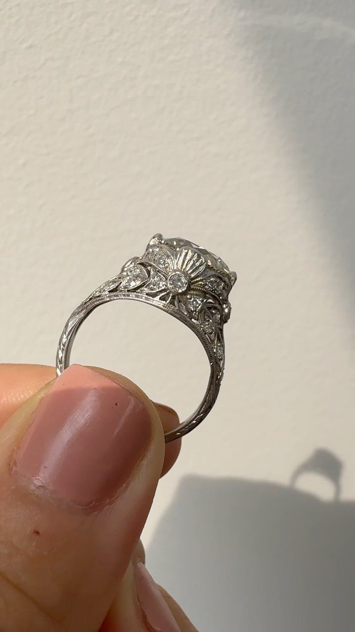 Vintage style diamond ring with ornate engravings held by a person's thumb.