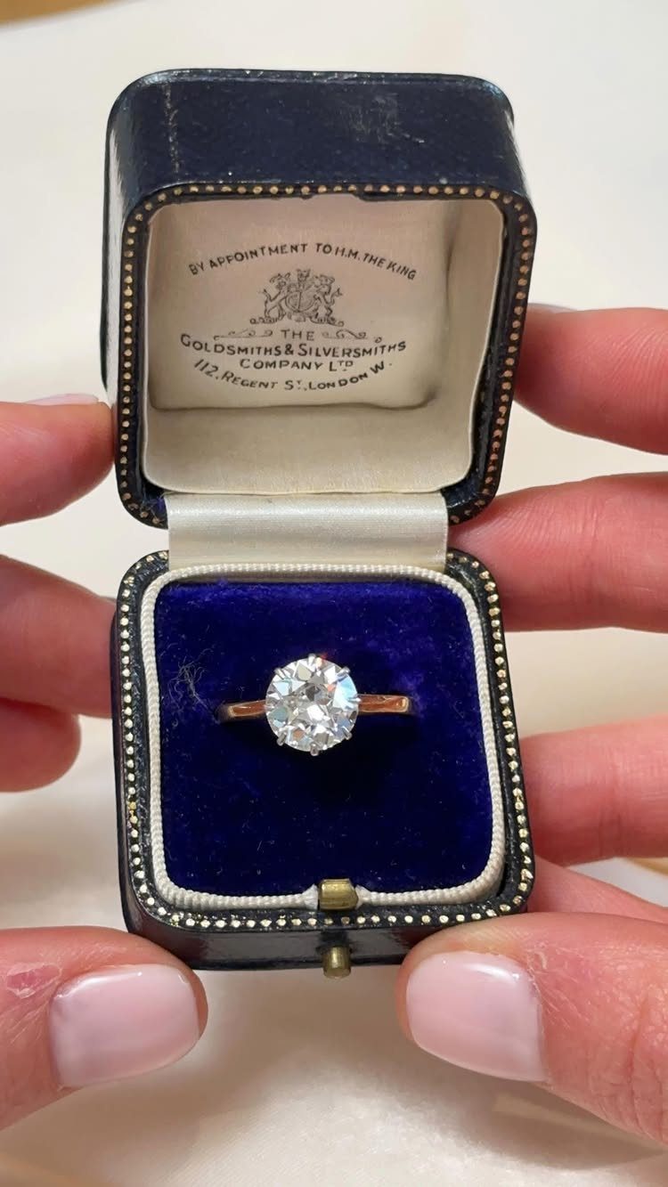 Gold diamond ring resting in a blue velvet vintage jewelry box held by hands