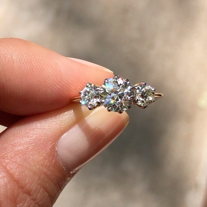 Gold ring with three round diamonds held between a person's fingers.