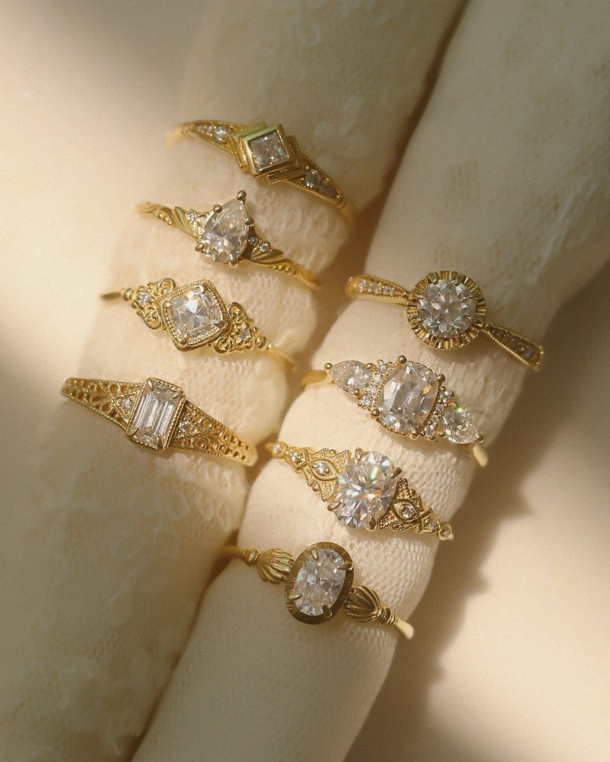 Various gold vintage engagement rings with different diamond settings on white fabric.