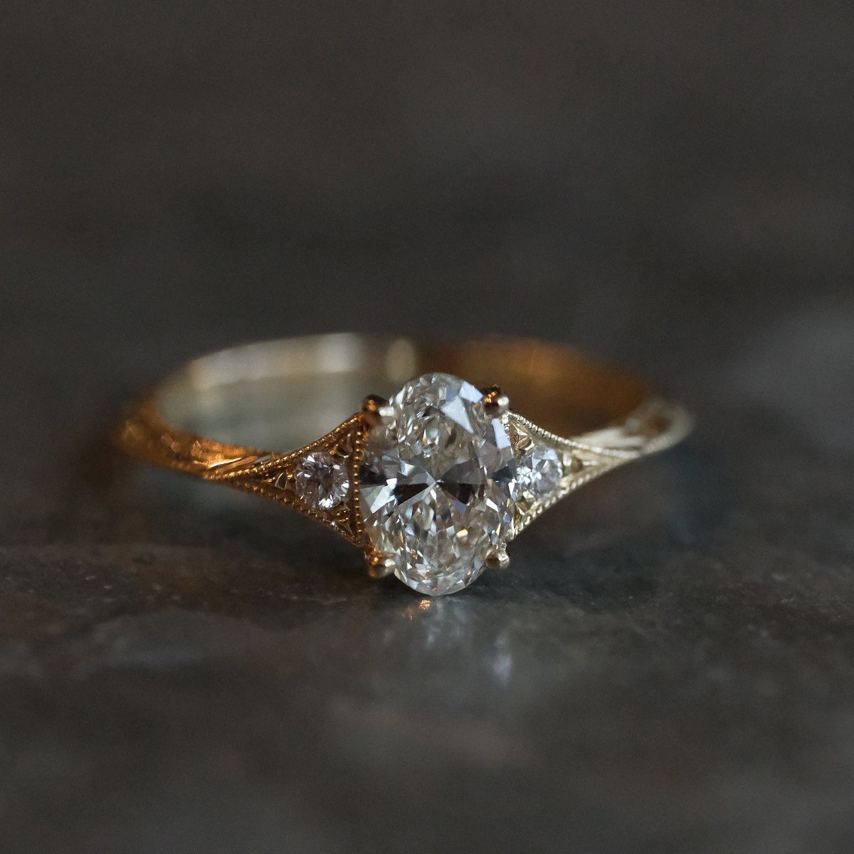 Gold engagement ring with oval diamond and filigree details on dark stone