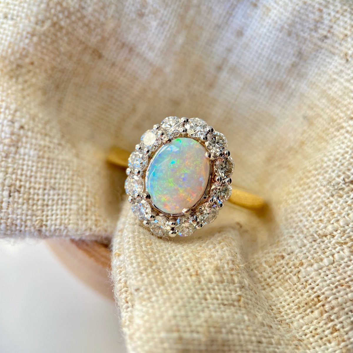 Gold ring with an oval opal center surrounded by a diamond cluster halo.
