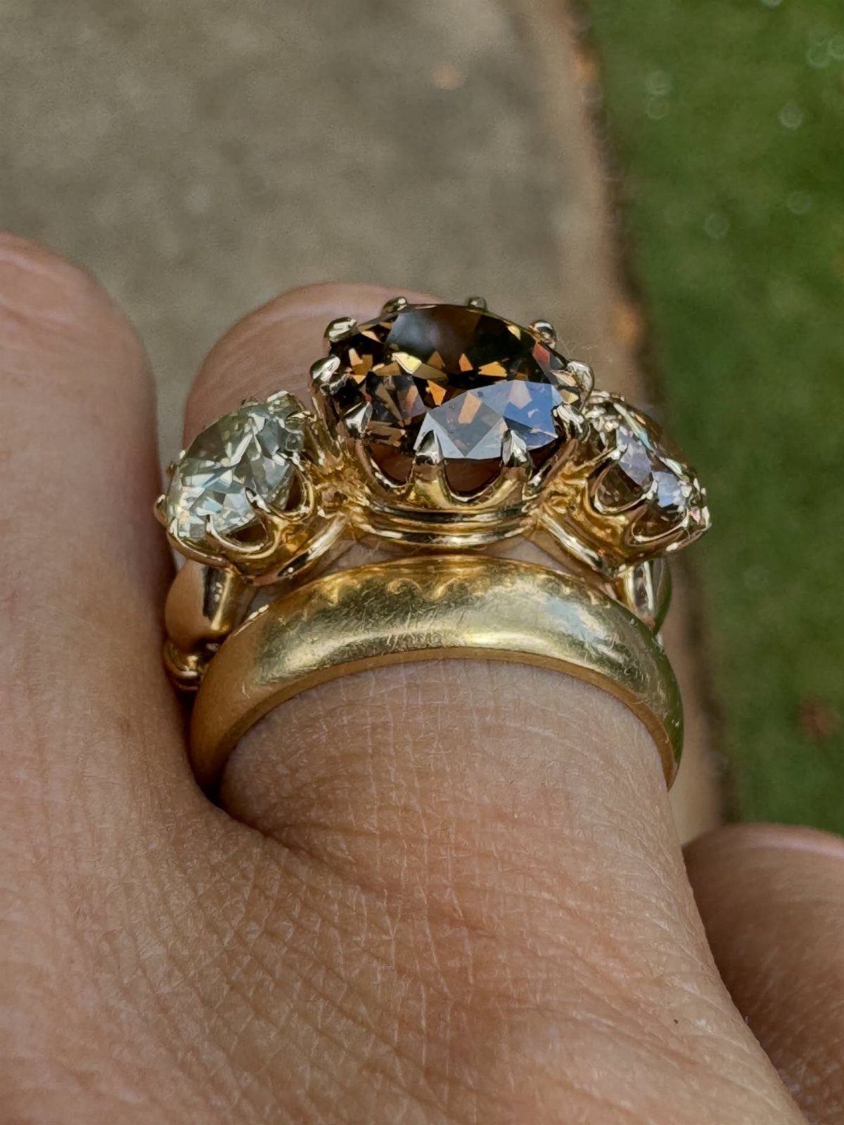 Three-stone gold ring with a brown center sapphire and side diamonds on finger