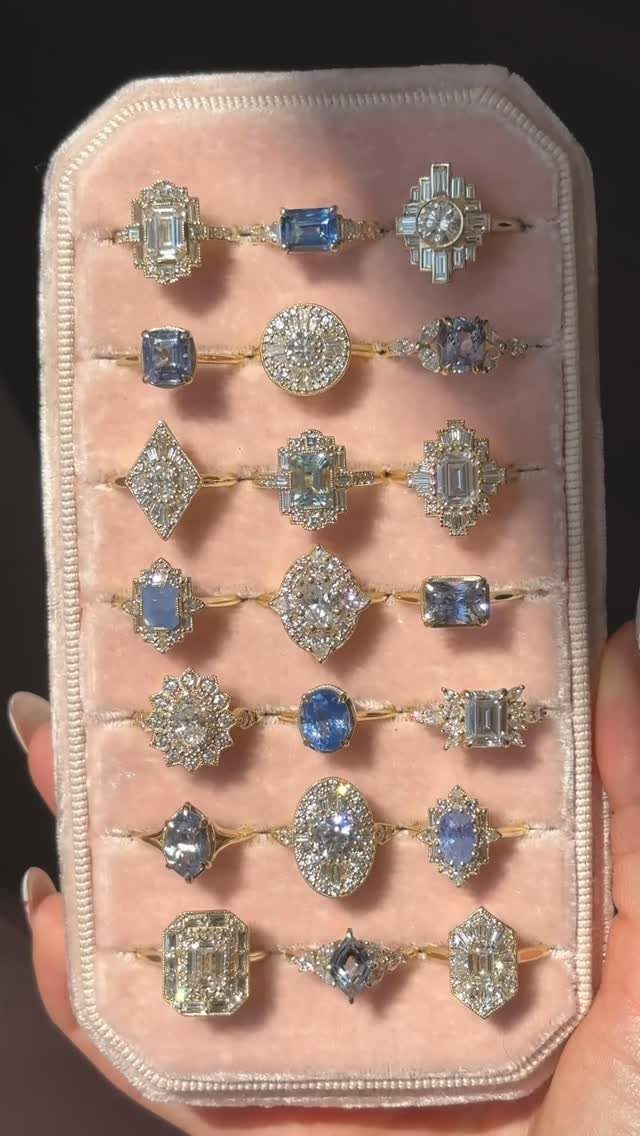 Various vintage style engagement rings with diamonds and blue gemstones on pink velvet.