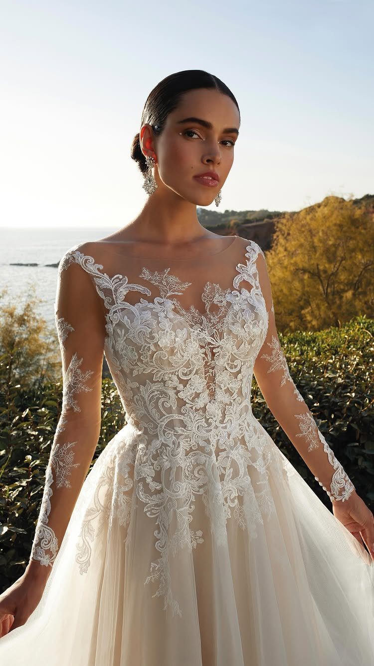 Woman in a white lace and tulle wedding dress with long sleeves outdoors.