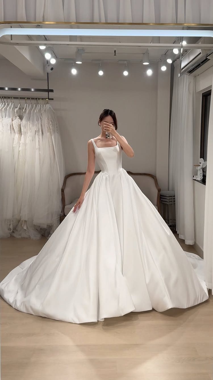 Woman wearing a voluminous white satin wedding gown in a bridal boutique.