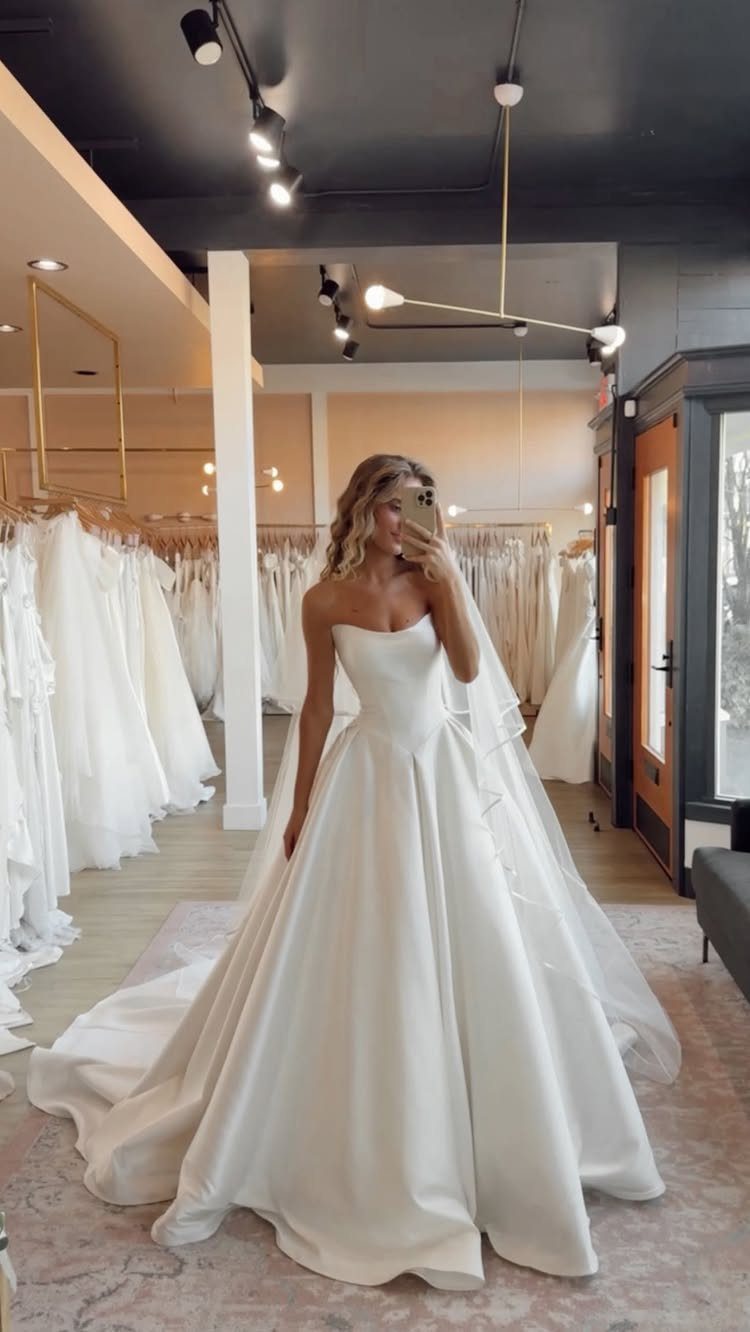 Woman in a strapless white satin A-line wedding gown posing in a bridal boutique.