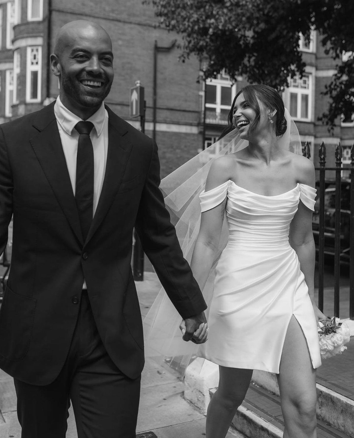 Smiling couple holding hands, woman wearing a short off-the-shoulder white wedding dress.