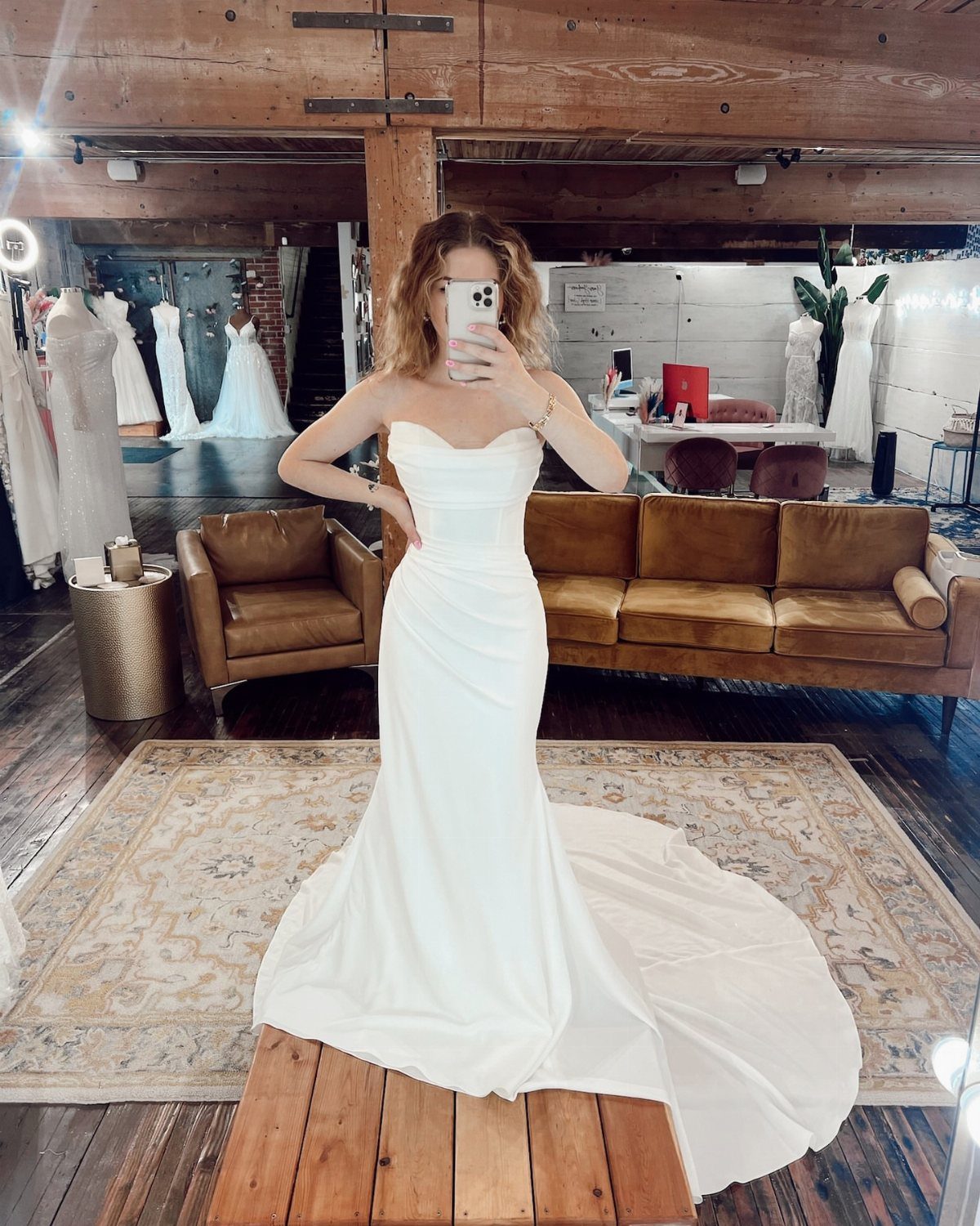 Woman in a strapless white column wedding gown posing in a bridal boutique.