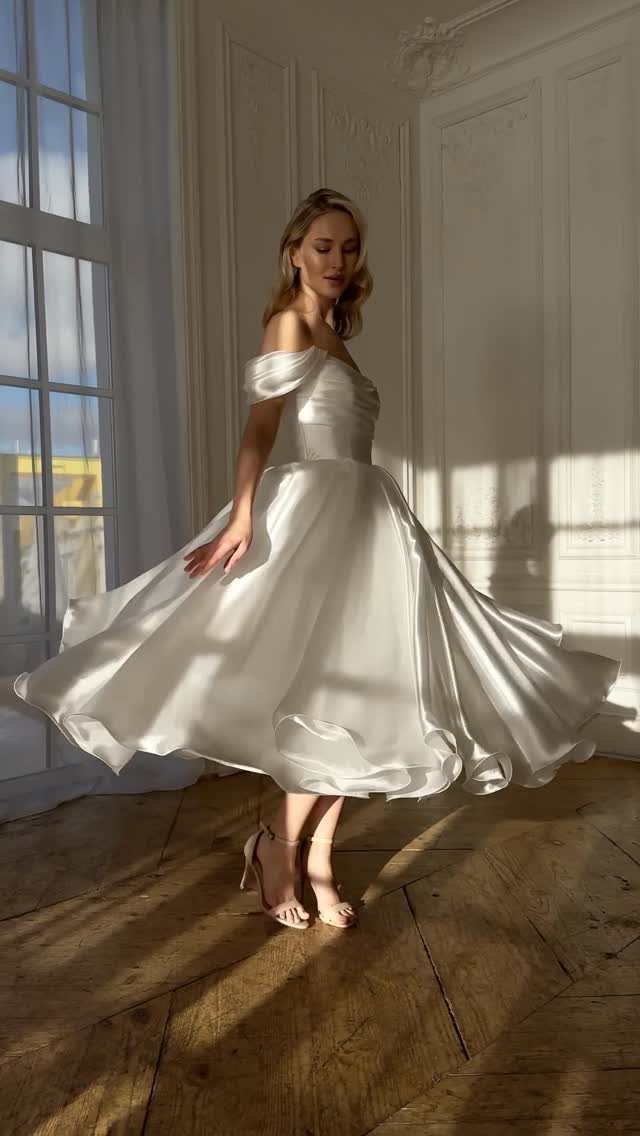 Woman in a white off-the-shoulder tea-length wedding dress posing in a bright room.