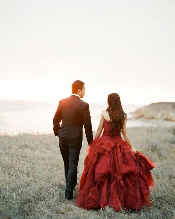 Couple walking in a field, woman wearing a voluminous red wedding dress.