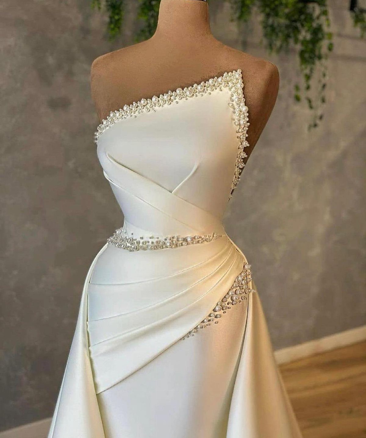 White satin wedding gown with pearl embellishments on a mannequin