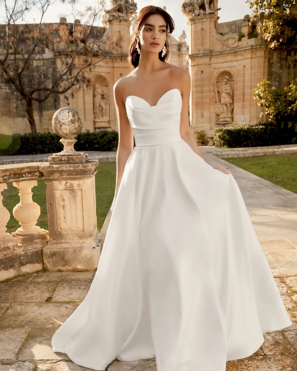 Woman in a strapless white A-line wedding dress standing by classical stone architecture.