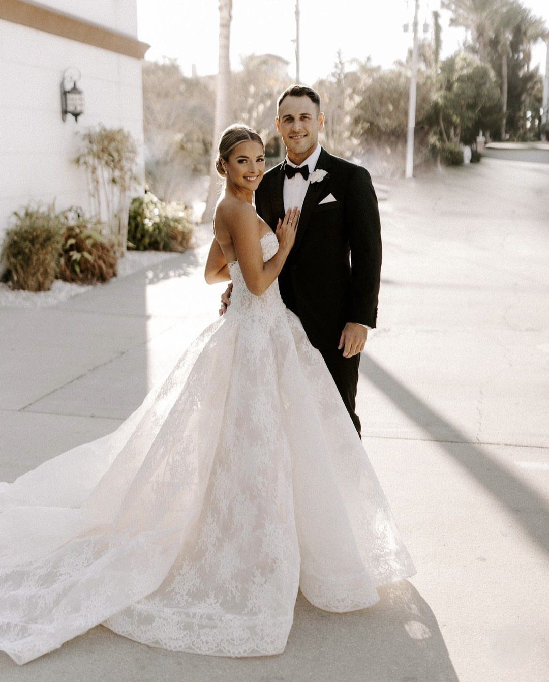 Bride in a strapless lace wedding gown and groom in a black tuxedo posing.