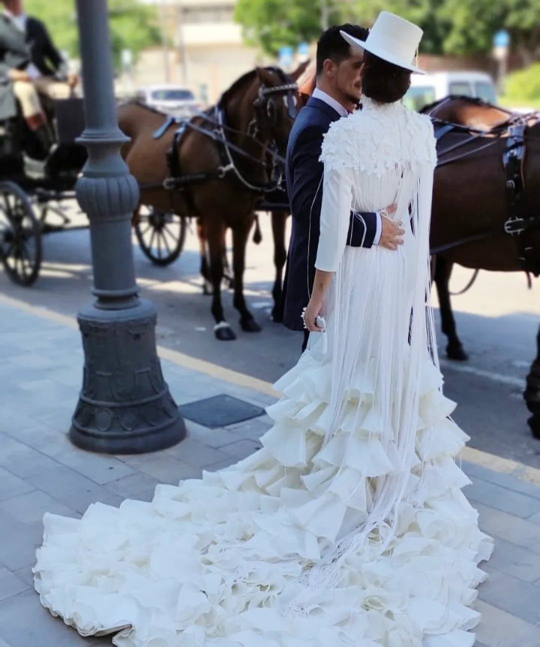 Woman in white flamenco style wedding dress with ruffles and fringe embracing a man.