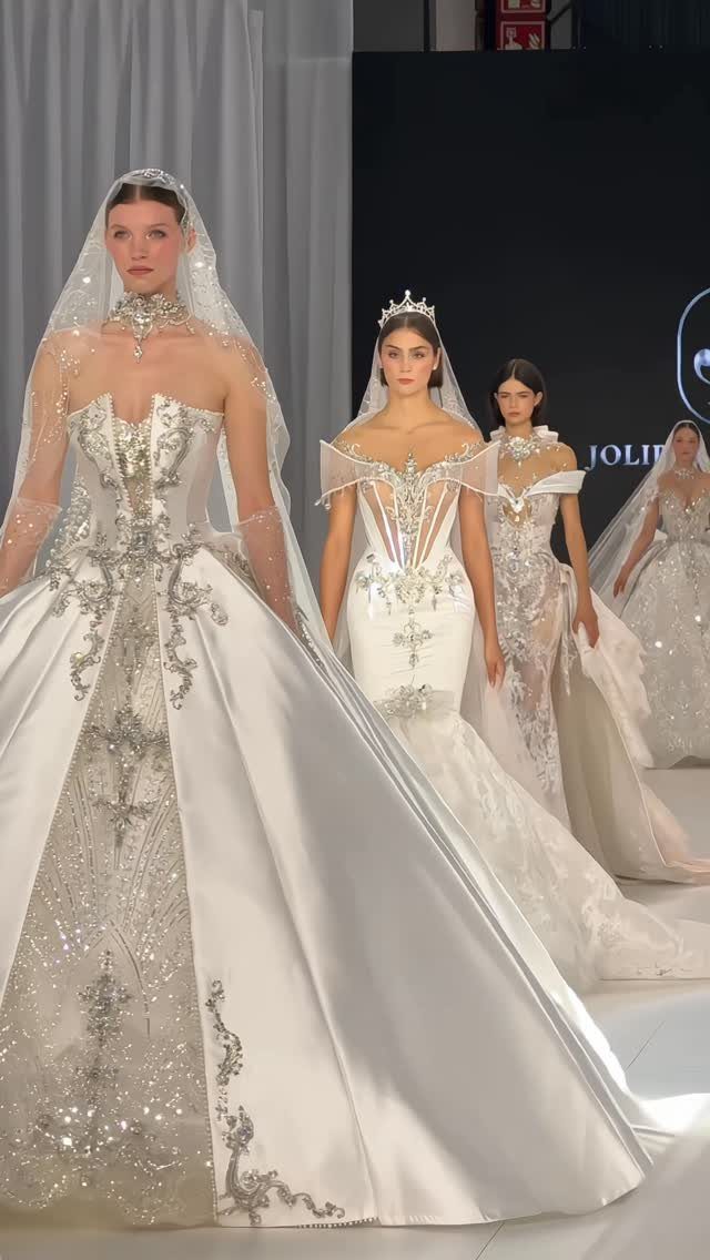 Models wearing ornate white wedding dresses with silver embroidery on a fashion runway