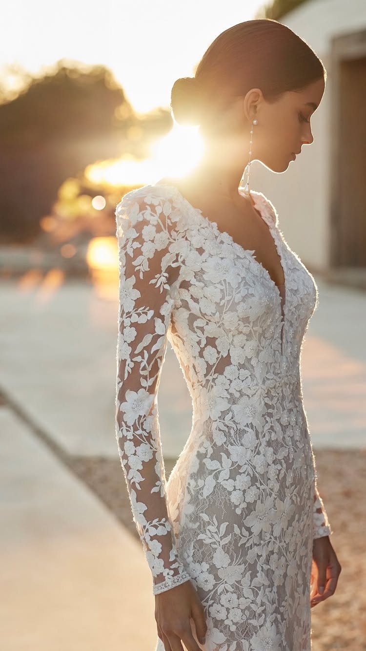 Woman in a white long-sleeved lace wedding dress posing during a golden sunset.