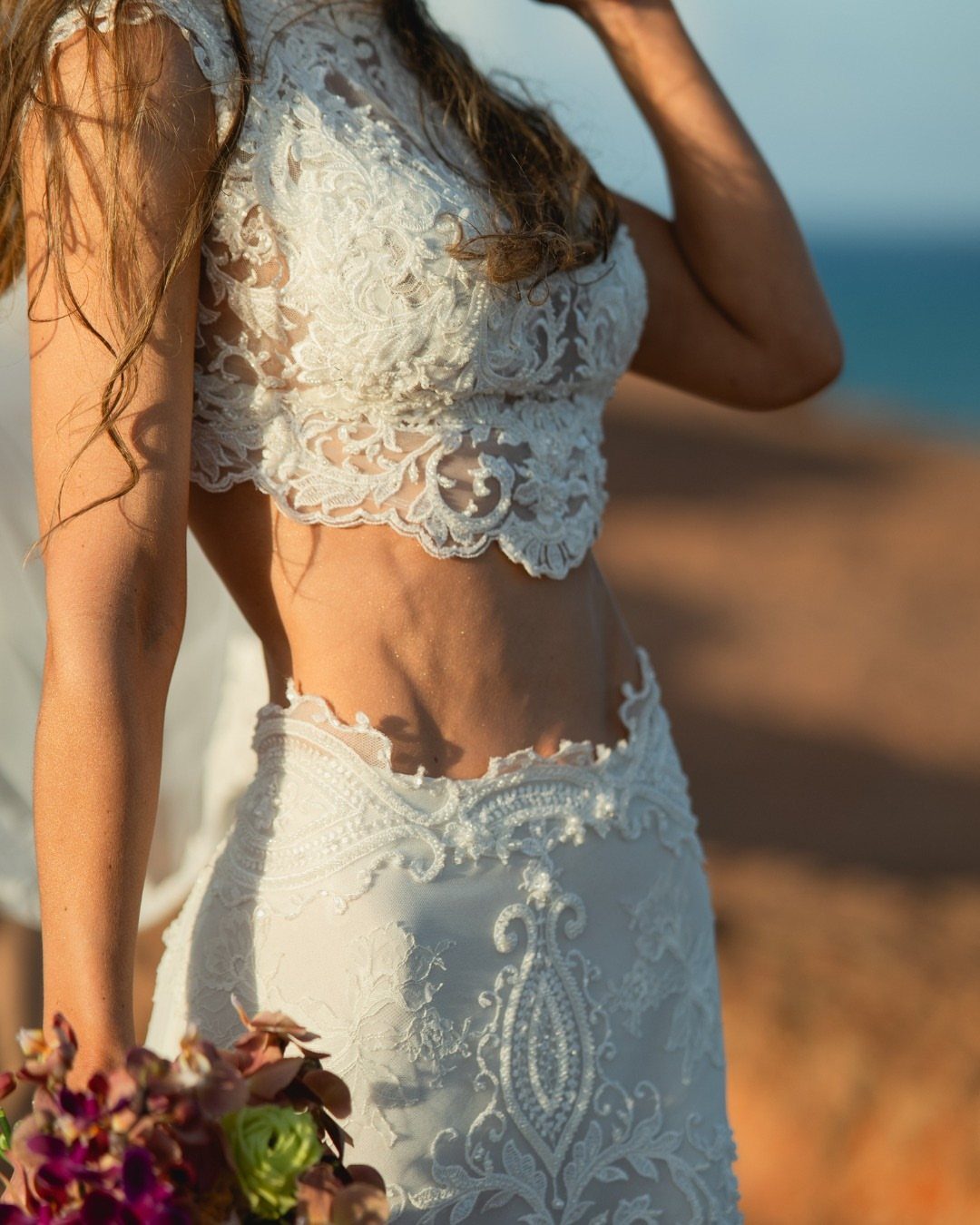 Woman in a white lace two-piece wedding dress holding a colorful floral bouquet.